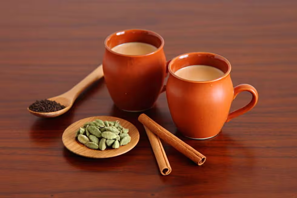 Tea in two earthen cups with cardamom and other spices on a wooden table